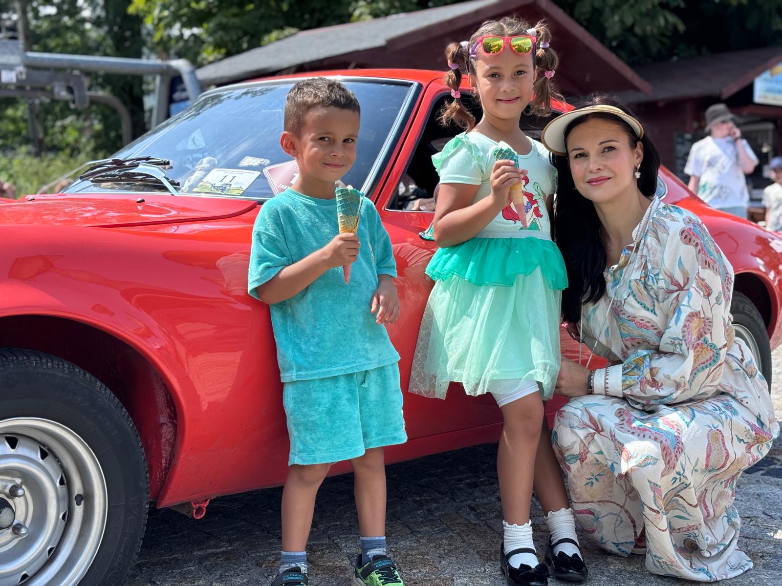 Two children with ice creams and their mother beside a red classic car, original photo