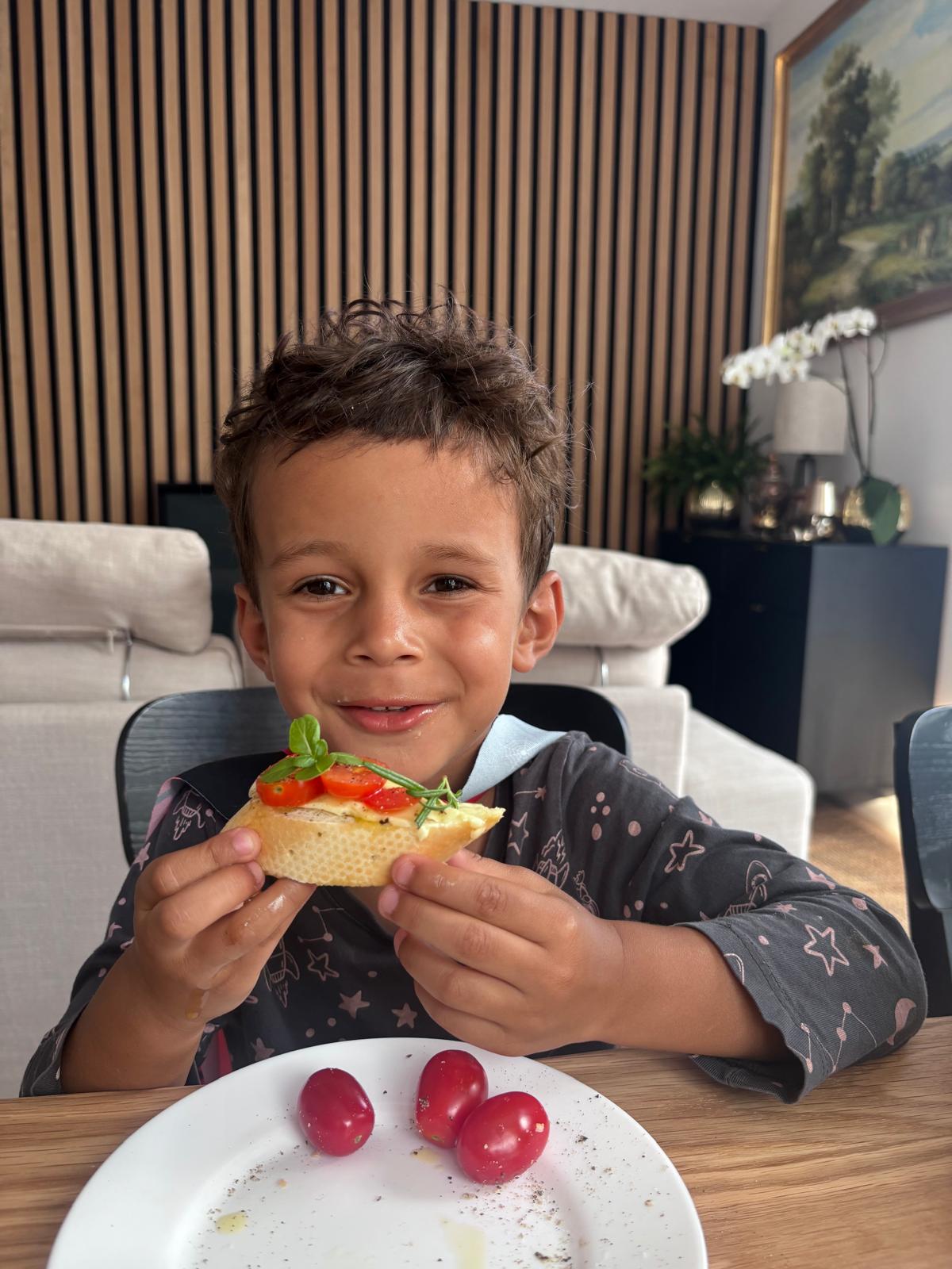 Boy at the table holding a slice of bruschetta, original photo